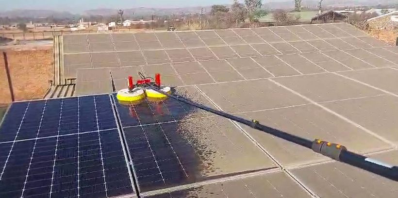 Rotating brush washing dusty solar panels on a large roof