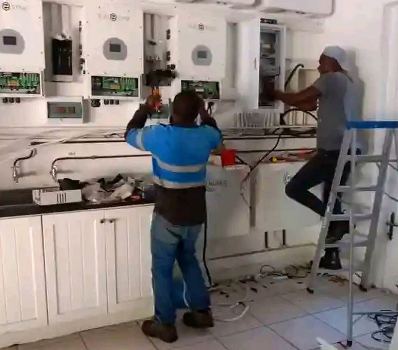 Two technicians wiring a row of hybrid inverters